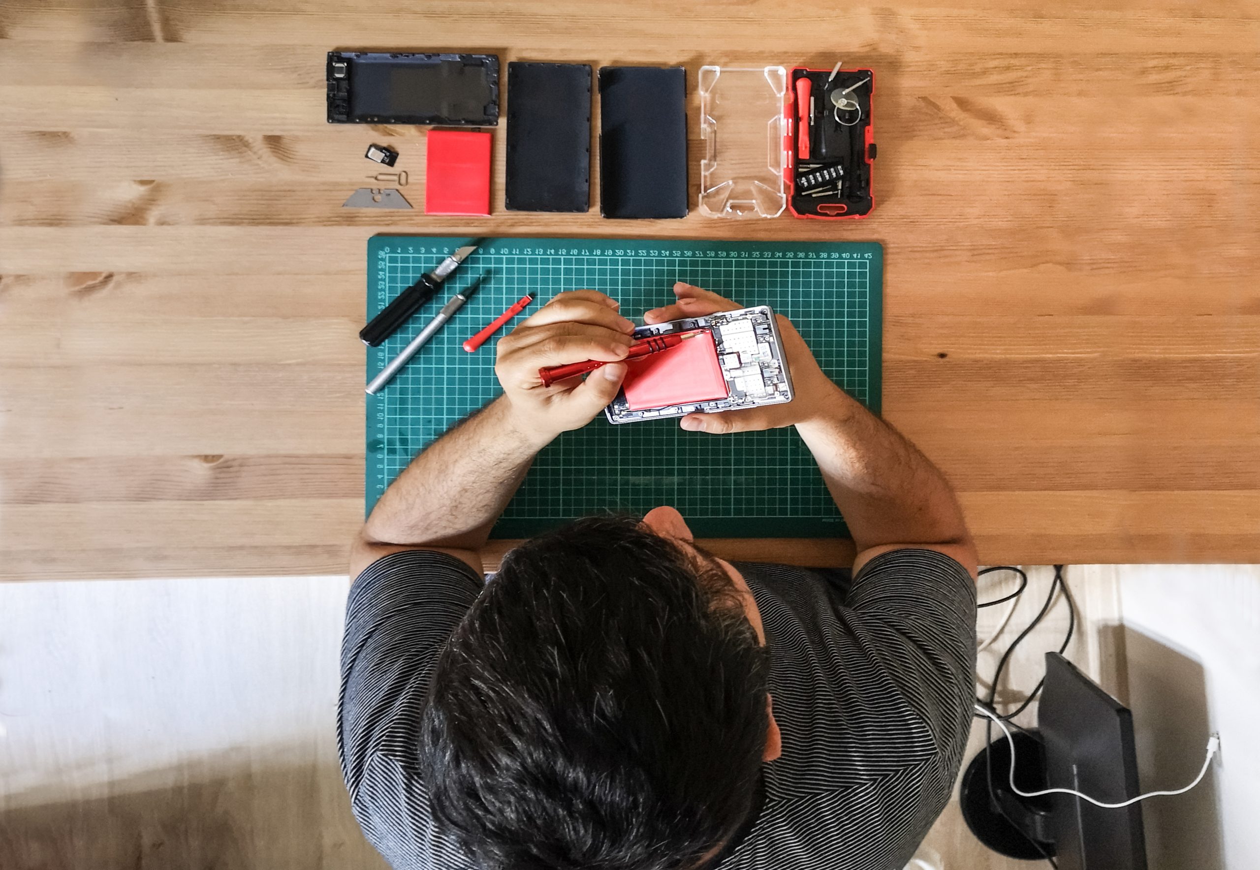 Technician repairing a smartphone with tools laid out on a workbench.