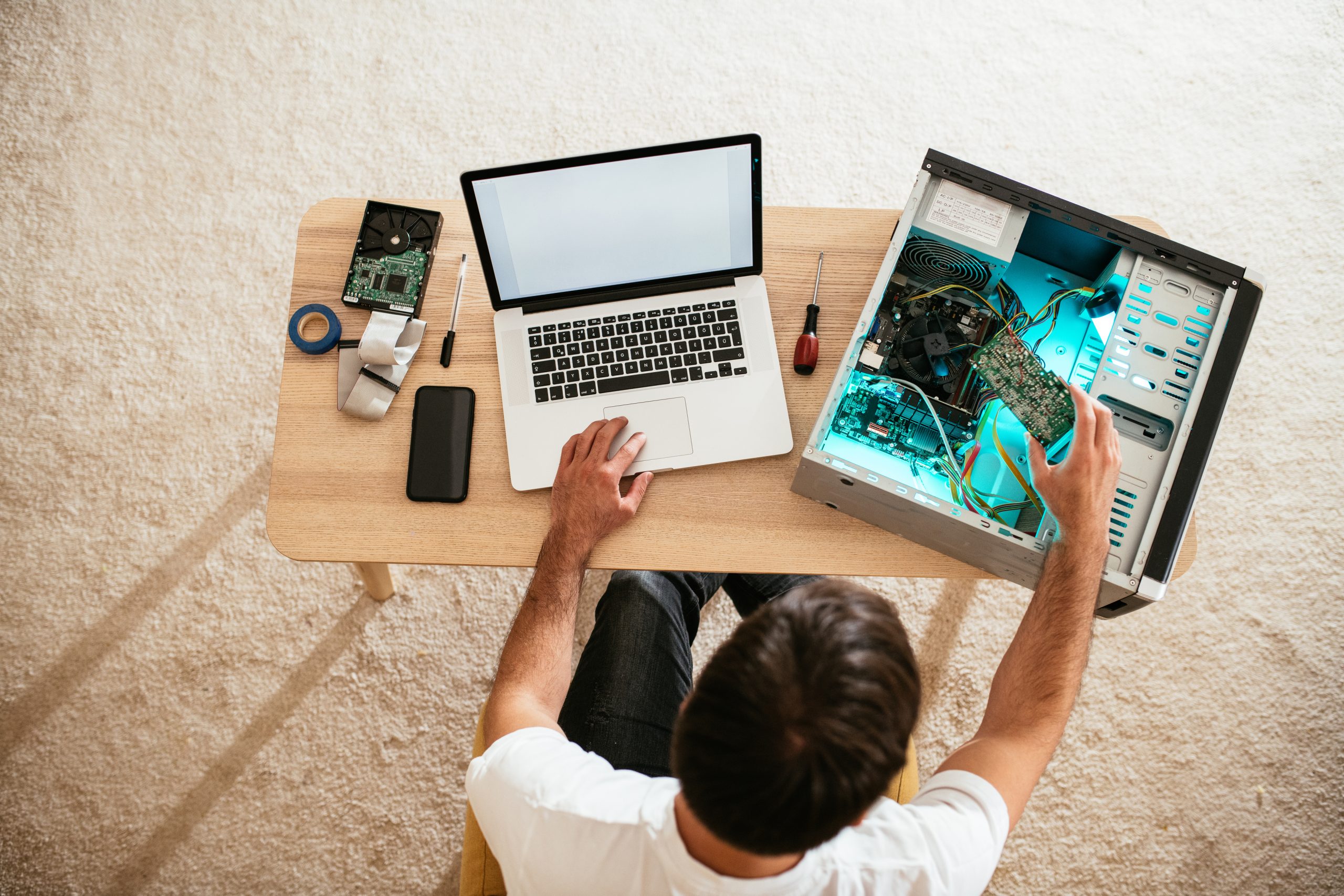 "A person working on data transfer between a laptop and a desktop computer, surrounded by tools and components.