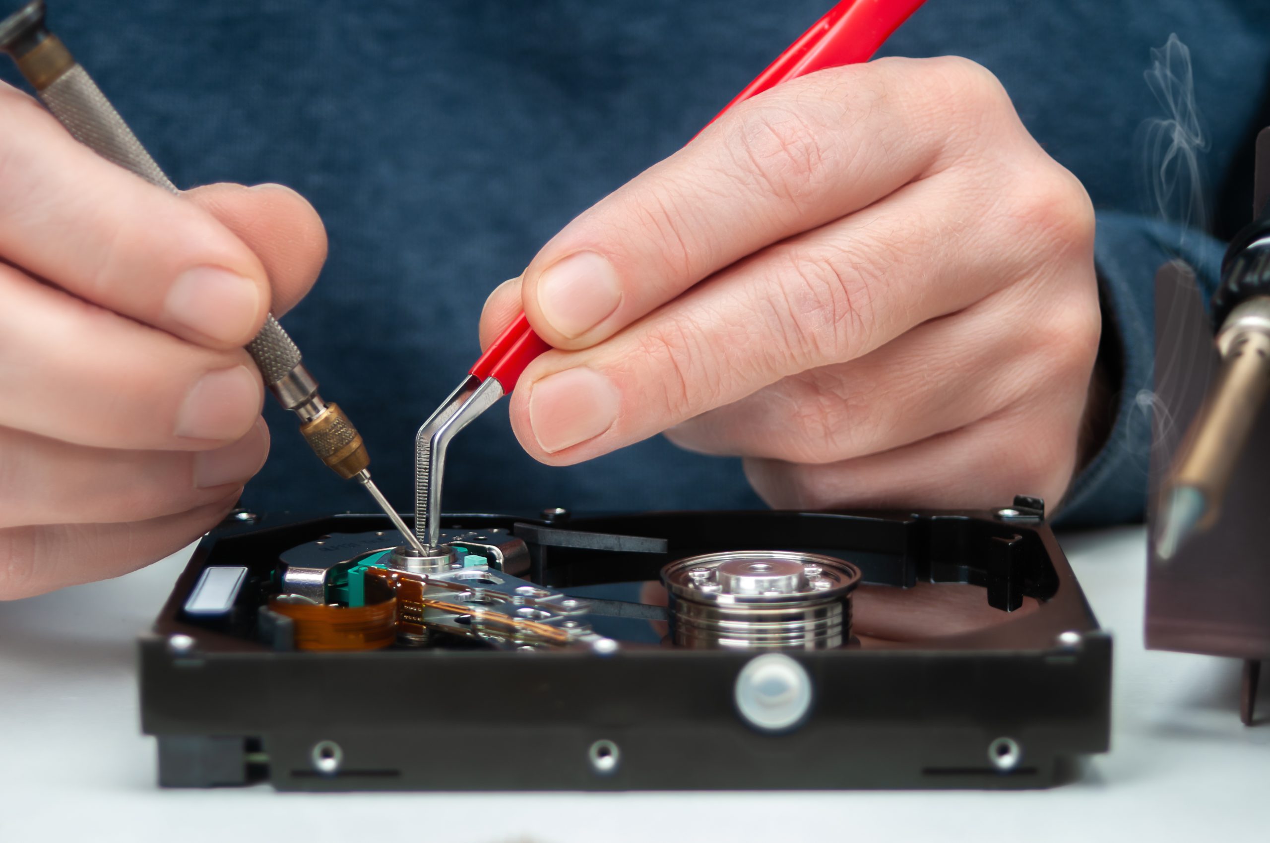 Close-up of a technician's hands repairing a hard drive in a workshop, symbolizing professional data recovery services.